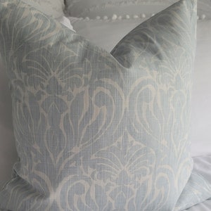 Könnte beinhalten: Ein hellblaues Kissen mit einem weißen Damastmuster. Das Kissen liegt auf einem weißen Bett.