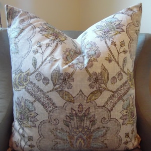 May include: A decorative cushion with a floral pattern in shades of beige, brown, purple, and blue. The cushion features a paisley design with intricate details.
