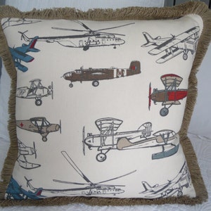 May include: A beige pillow with a brown fringe border features a repeating pattern of vintage airplanes in various colors and styles.