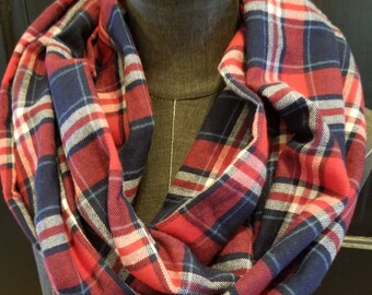 Könnte beinhalten: Ein roter, marineblauer und weiß karierter Loop-Schal auf einer Schaufensterpuppe. Der Schal ist aus einem weichen Stoff gefertigt und um den Hals der Schaufensterpuppe gewickelt. Das Karomuster ist ein klassisches Design.