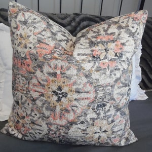 May include: A decorative throw pillow with a floral pattern in shades of gray, pink, and beige. The pillow has a square shape and a soft, textured fabric.