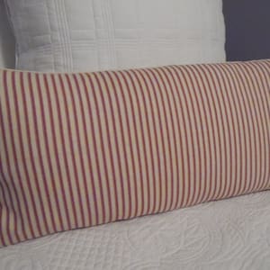 May include: A striped cushion with red and white stripes. The cushion is made of a soft, woven fabric and has a rectangular shape.