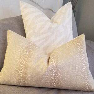 Puede incluir: Dos almohadas decorativas, una con estampado de cebra blanco y beige y la otra con un patr&oacute;n moteado beige y blanco.