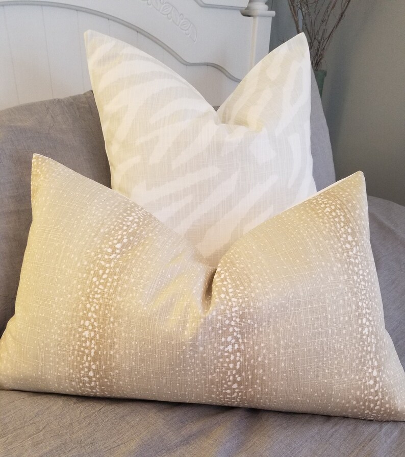 Puede incluir: Dos almohadas decorativas, una con estampado de cebra blanco y beige y la otra con un patr&oacute;n moteado beige y blanco.