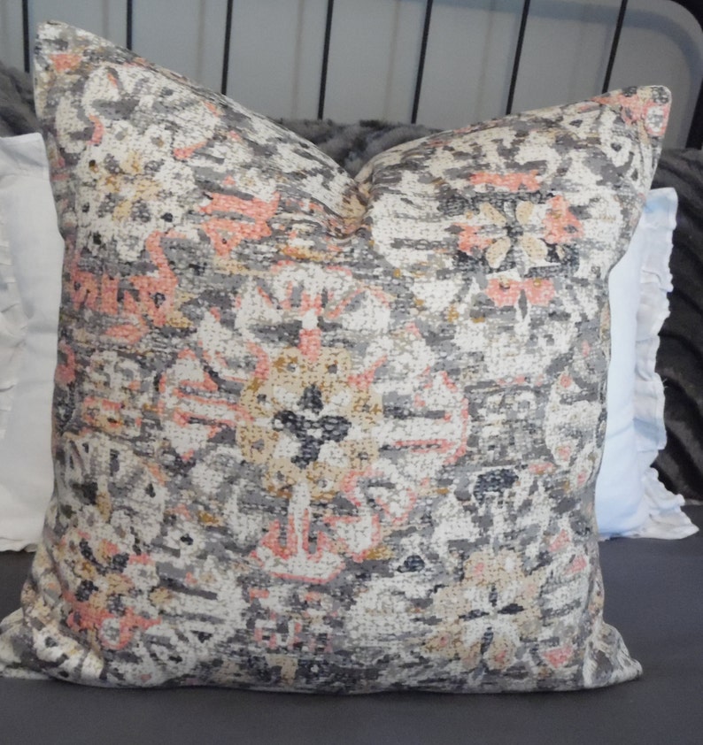 May include: A decorative throw pillow with a gray, pink, and beige floral pattern. The pillow is made of a soft, textured fabric.