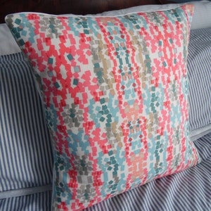 May include: A square throw pillow with a geometric pattern in shades of pink, teal, gray, and white.