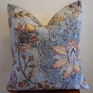 May include: A blue and beige throw pillow with a floral pattern. The pillow features a large floral design with shades of blue, beige, orange, and red.