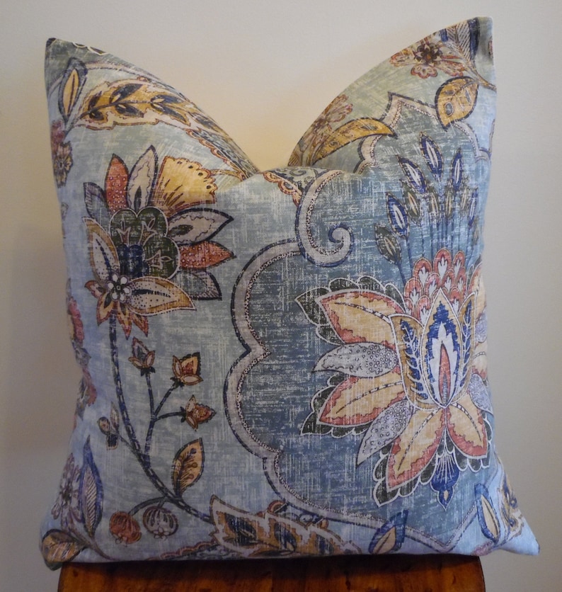 May include: A blue and beige throw pillow with a floral pattern. The pillow features a large floral design with shades of blue, beige, orange, and red.