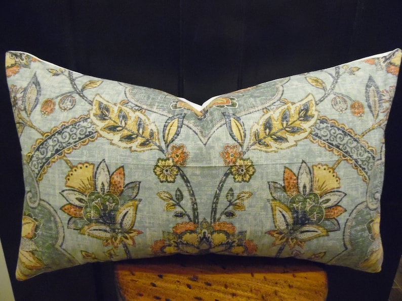 May include: A decorative cushion with a blue background and a floral pattern in shades of yellow, orange, and green. The cushion has a white border.