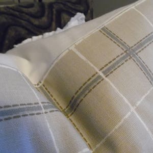 May include: Two pillowcases with a plaid pattern in shades of beige, brown, and blue. The pillowcases are made of a soft, woven fabric.