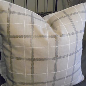 May include: A beige pillow with a white and brown plaid pattern. The pillow has a ruffled edge.