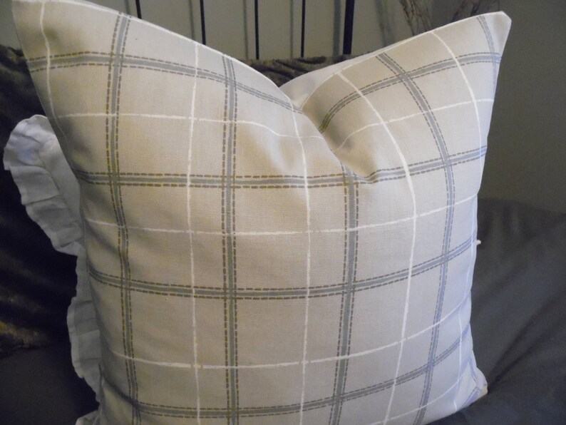 May include: A beige pillow with a white and brown plaid pattern. The pillow has a ruffled edge.