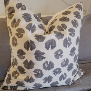 Puede incluir: Una almohada blanca con un patrón de hojas grises. La almohada está hecha de una tela suave y texturizada.