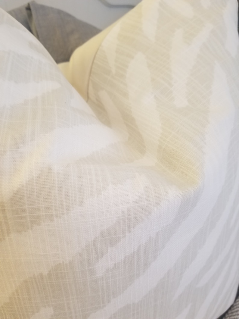 Puede incluir: Una almohada blanca con un sutil estampado de cebra marr&oacute;n claro. La tela tiene una textura similar al lino.