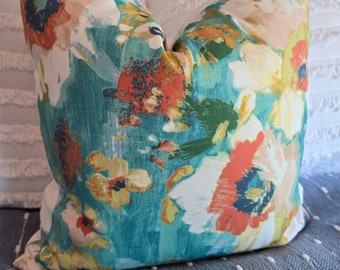 May include: A teal blue throw pillow with a floral pattern featuring orange, yellow, and white flowers. The pillow has a soft, textured fabric.