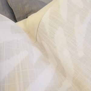 Puede incluir: Una almohada blanca con un sutil patr&oacute;n ikat gris. La almohada est&aacute; hecha de una tela suave y texturizada.