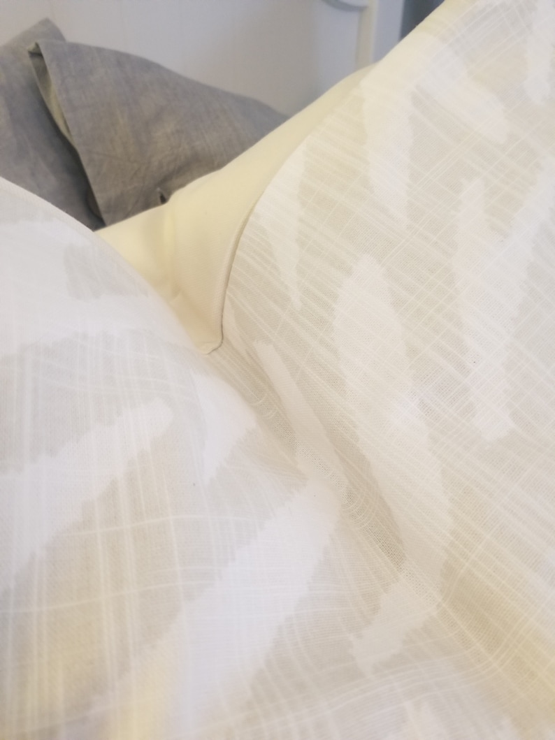 Puede incluir: Una almohada blanca con un sutil patr&oacute;n ikat gris. La almohada est&aacute; hecha de una tela suave y texturizada.