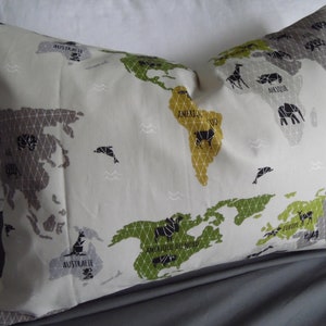 Può includere: Un cuscino bianco con un disegno di mappa del mondo stampato su di esso. La mappa è in tonalità di grigio, verde e giallo. I continenti sono etichettati con i loro nomi in testo nero. Il cuscino ha un bordo arricciato.