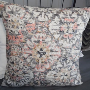 May include: A decorative throw pillow with a gray, pink, and beige patterned design. The pattern features intricate floral and geometric shapes.