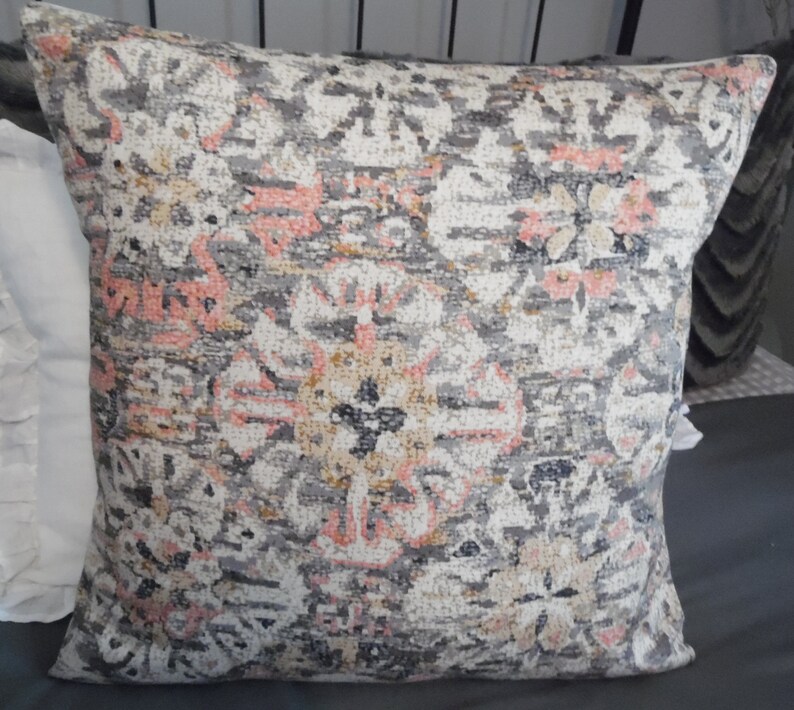May include: A decorative throw pillow with a gray, pink, and beige patterned design. The pattern features intricate floral and geometric shapes.