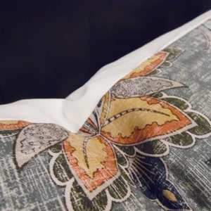 May include: A close-up of a cushion with a blue, green, orange and yellow floral pattern. The cushion has a white border.