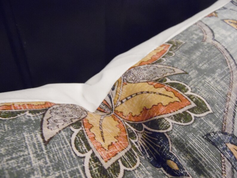 May include: A close-up of a cushion with a blue, green, orange and yellow floral pattern. The cushion has a white border.