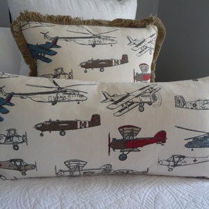 May include: Two decorative throw pillows with a fringe border. The pillows are made of a white fabric with a pattern of various airplanes in black, red, blue, and brown.