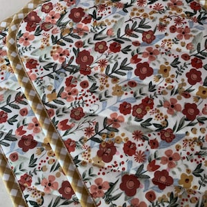 May include: Two quilted pot holders with a floral pattern in shades of red, pink, and yellow. The pot holders have a yellow and white checkered border.