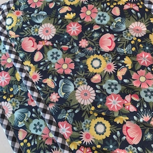 May include: Floral quilted placemats with a dark blue background, featuring pink, yellow, and blue flowers, and butterflies. The edges are trimmed with a black and white checkered pattern.