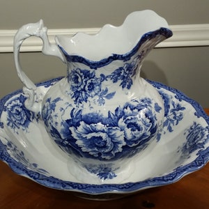May include: A white porcelain pitcher and bowl set with a blue and white floral pattern. The pitcher has a decorative handle and a scalloped rim. The bowl has a scalloped edge and a blue and white floral border.