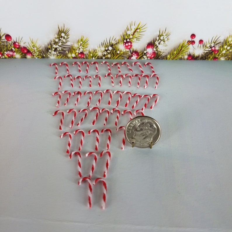 May include: A large quantity of miniature candy canes, arranged in a fan shape, with a US dime for scale. The candy canes are red and white.