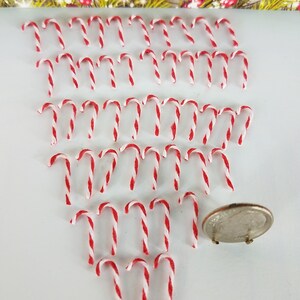 May include: A large quantity of miniature candy canes, approximately 40, in red and white, arranged in a triangular pattern on a white surface. A US quarter is included for scale.