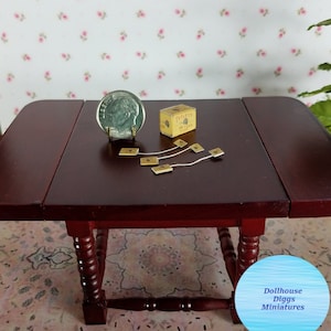 May include: A miniature dollhouse tea set with a box of Tetley's tea bags, a small plate, and four tea bags on a wooden table.