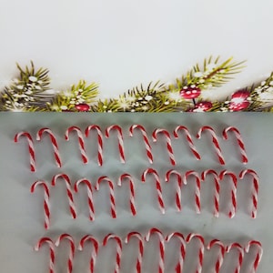 May include: A collection of red and white candy canes arranged in rows on a white surface. The candy canes are all the same size and shape.