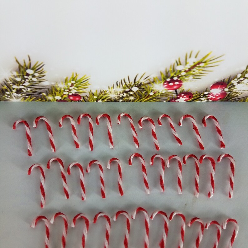May include: A collection of red and white candy canes arranged in rows on a white surface. The candy canes are all the same size and shape.