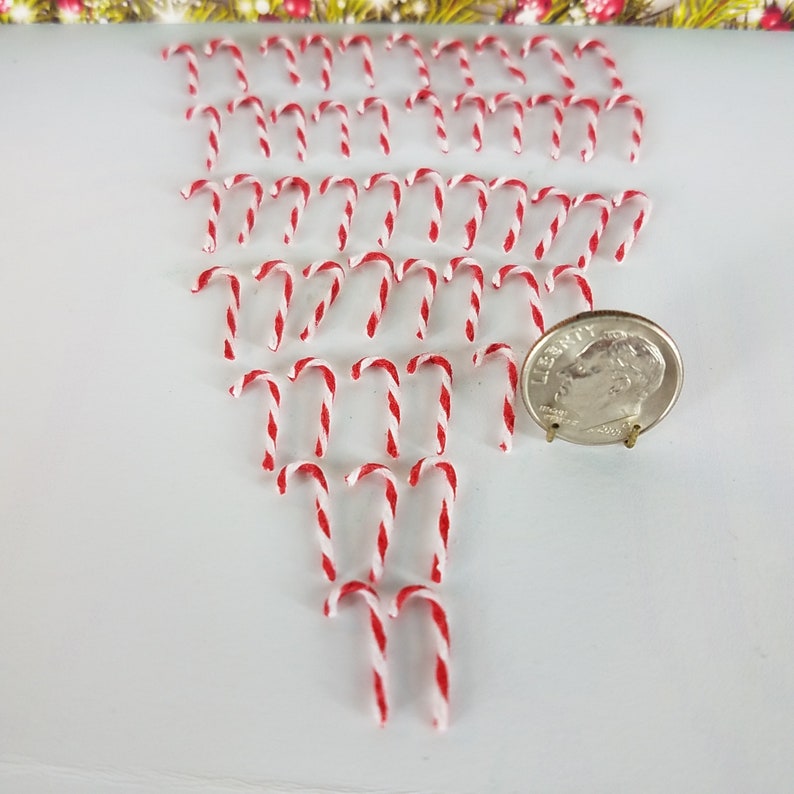 May include: A collection of miniature red and white candy canes arranged in a triangular pattern on a white surface. A US dime is included for scale.