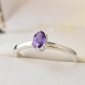 May include: A silver ring with a purple gemstone set in a prong setting.