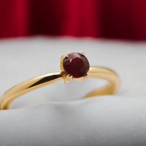 May include: A gold ring with a dark red gemstone set in the center.