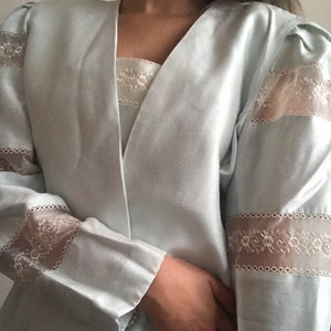 May include: A light blue blazer with long sleeves and a V-neck. The sleeves and neckline are trimmed with white lace.
