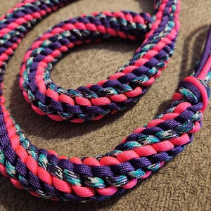 May include: A brightly coloured braided rope, featuring pink, purple, and teal strands. The rope is tightly woven, creating a thick, durable texture. The colours are vibrant and eye-catching, with a mix of solid and patterned sections. Likely used for crafting or pet accessories.