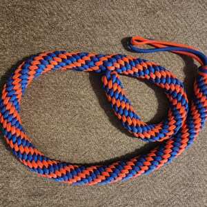 May include: A braided rope in a circular form, with a striking pattern of alternating blue and orange strands. The rope has a loop at one end and a smaller loop at the other, possibly for a handle or attachment.
