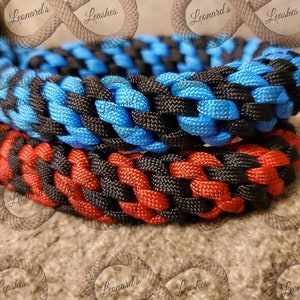 May include: Close-up of two braided dog leads. One is red and black, the other is blue and black. The leads are made of a durable material and are tightly woven. The brand name "Leonard's Leashes" is visible in the background.