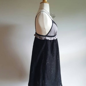 K&ouml;nnte beinhalten: Ein schwarzes Spitzenkleid mit grauer Unterlage und einem R&uuml;schenbesatz. Das Kleid befindet sich auf einer wei&szlig;en Schaufensterpuppe.