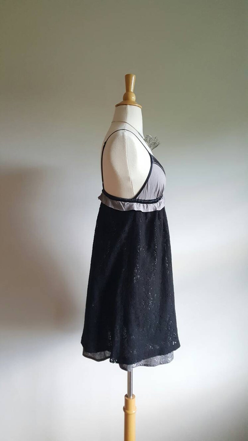 K&ouml;nnte beinhalten: Ein schwarzes Spitzenkleid mit grauer Unterlage und einem R&uuml;schenbesatz. Das Kleid befindet sich auf einer wei&szlig;en Schaufensterpuppe.