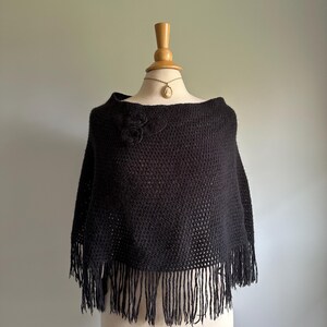 May include: Black crochet poncho with a fringe border and a flower detail on the shoulder.