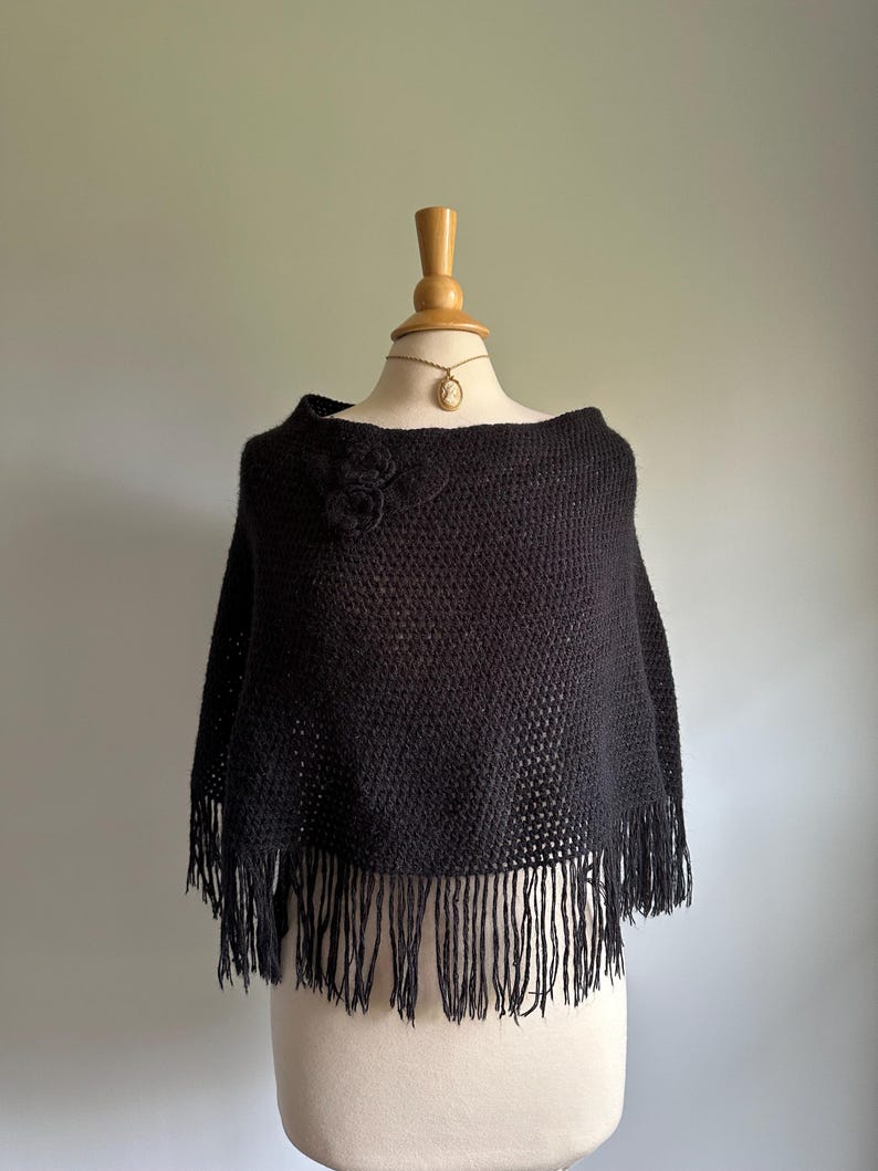 May include: Black crochet poncho with a fringe border and a flower detail on the shoulder.