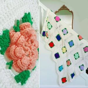 May include: A white crocheted blanket with a scalloped edge and colorful crocheted flowers. The blanket is draped over a white railing.