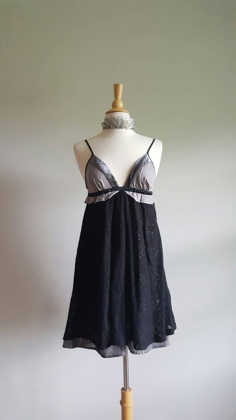 K&ouml;nnte beinhalten: Ein schwarzes Spitzenkleid mit einem grauen und schwarzen Samt-Oberteil. Das Kleid hat einen V-Ausschnitt und Spaghetti-Tr&auml;ger.