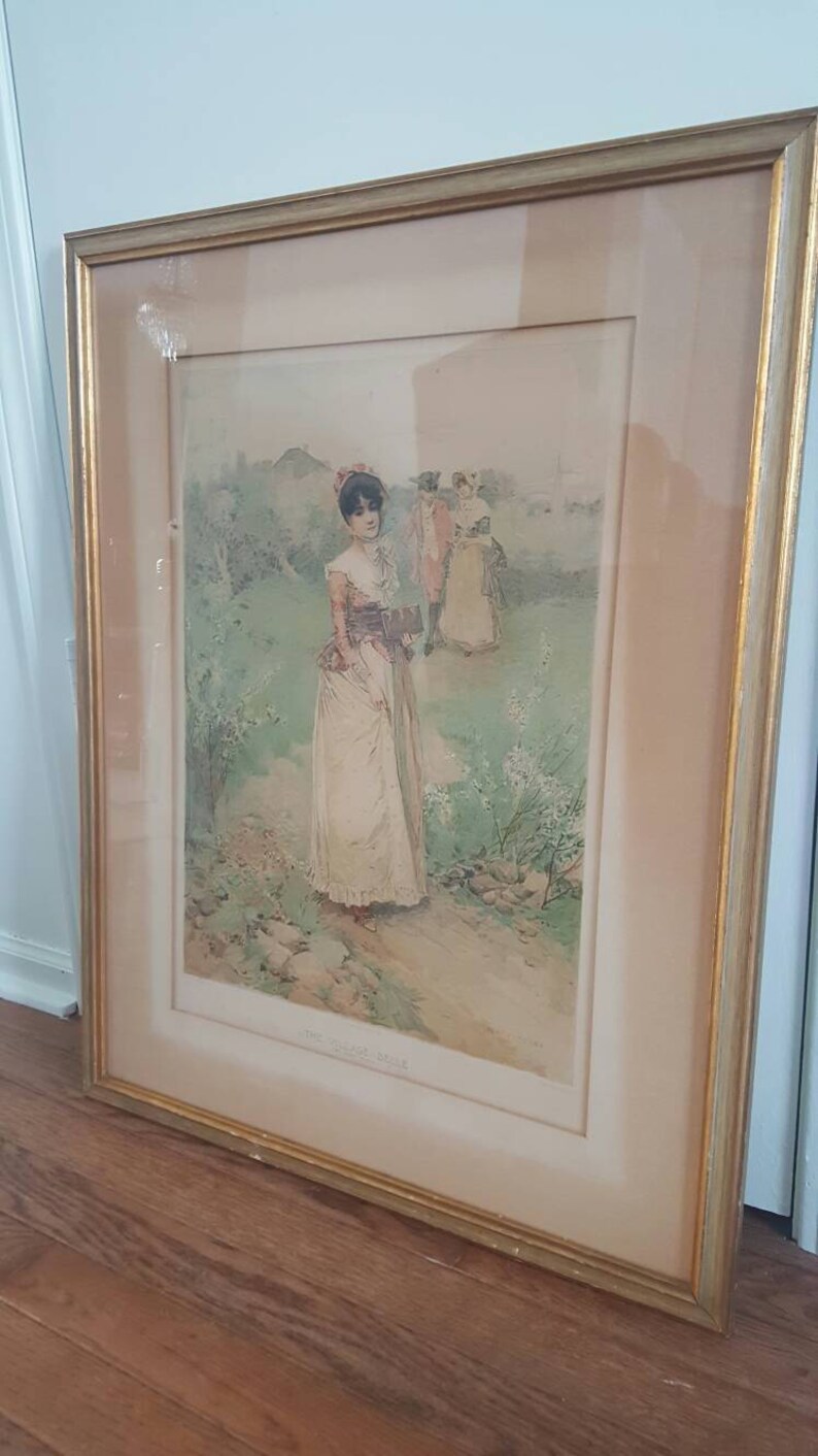 Puede incluir: Una impresi&oacute;n enmarcada de una mujer con un vestido blanco caminando por un jard&iacute;n. La impresi&oacute;n est&aacute; en un marco dorado y tiene un passe-partout blanco. El t&iacute;tulo de la impresi&oacute;n es "The Garden Gate".