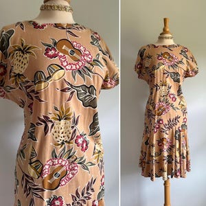 Peut inclure: Robe beige à imprimé tropical avec ananas, ukulélés et fleurs. La robe a des manches courtes et une jupe mi-longue. Le tissu est orné d'éléments marron, verts, jaunes et roses. La robe est présentée sur un mannequin.